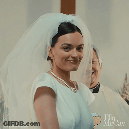 A Woman In A Wedding Dress With A Veil And A Pearl Necklace GIF