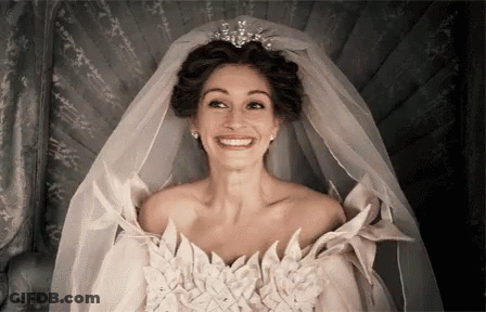 A Woman In A Wedding Dress With A Veil And Tiara Is Smiling . GIF