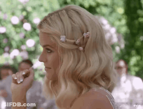 A Woman In A Wedding Dress With Flowers In Her Hair Is Sitting At A Table . GIF