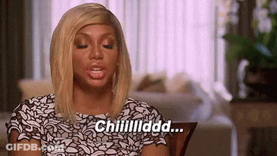 A Woman In A White And Black Dress Is Sitting In A Living Room Talking . GIF