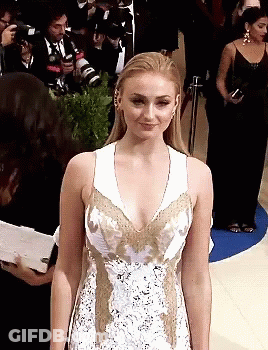 A Woman In A White And Gold Dress Stands In Front Of Photographers GIF
