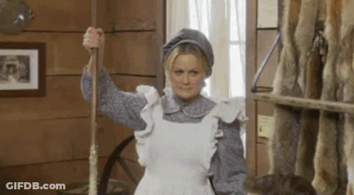 A Woman In A White Apron Is Holding A Mop In A Room . GIF