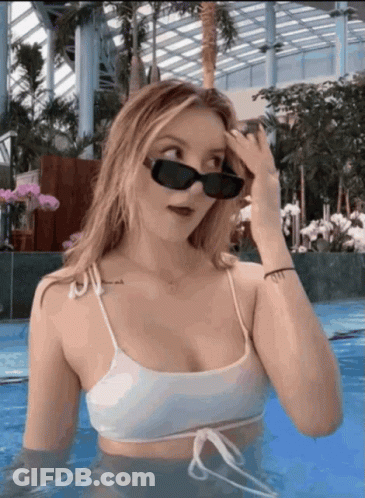 A Woman In A White Bikini And Sunglasses Is Standing In A Pool GIF