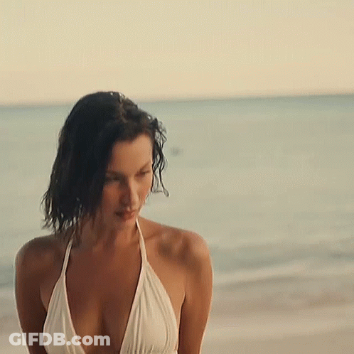 A Woman In A White Bikini Is Standing On The Beach Near The Ocean . GIF