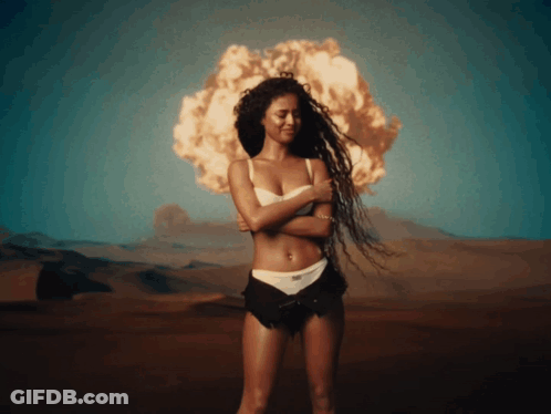 A Woman In A White Bra And Black Shorts Is Standing In Front Of An Explosion GIF