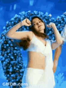 A Woman In A White Bra And White Skirt Is Dancing In Front Of A Flower Arrangement . GIF