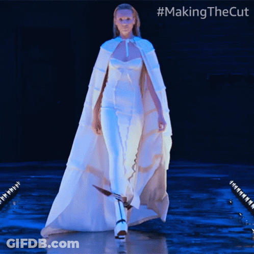 A Woman In A White Cape Is Walking Down A Runway With #Makingthecut Written On The Bottom GIF