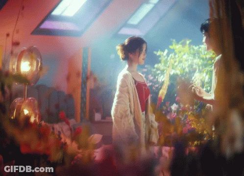 A Woman In A White Cardigan Stands Next To A Woman In A Red Top GIF