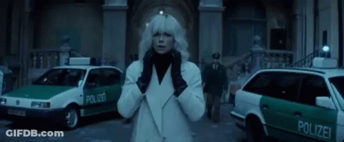 A Woman In A White Coat And Black Gloves Is Standing In Front Of A Group Of Police Cars . GIF