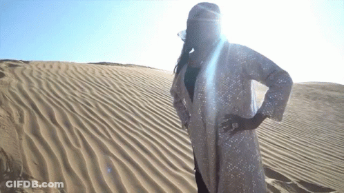 A Woman In A White Coat Stands In The Sand GIF