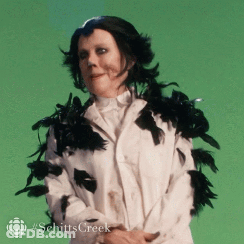 A Woman In A White Coat With Black Feathers Around Her Neck And Collar GIF