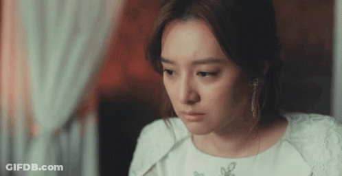 A Woman In A White Dress And Earrings Is Looking Down GIF