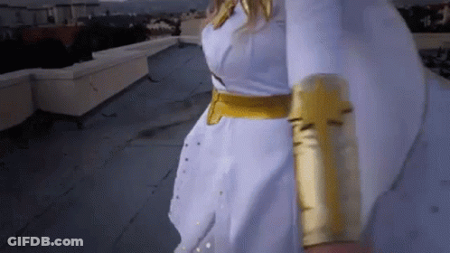 A Woman In A White Dress And Gold Gloves Is Walking On A Rooftop . GIF