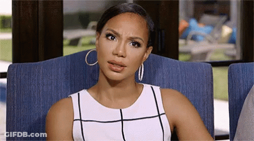 A Woman In A White Dress And Hoop Earrings Is Sitting In A Chair And Making A Funny Face . GIF
