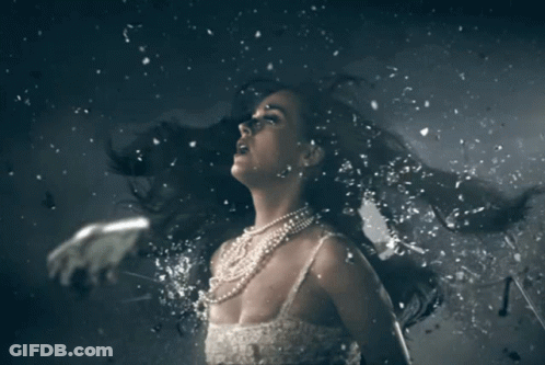 A Woman In A White Dress And Pearls Is Surrounded By Pieces Of Glass GIF