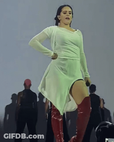 A Woman In A White Dress And Red Boots Is Standing On A Stage GIF