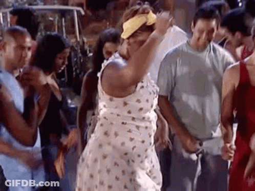 A Woman In A White Dress And Yellow Headband Is Dancing In A Crowd Of People . GIF