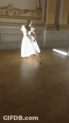 A Woman In A White Dress Dancing On A Wooden Floor GIF