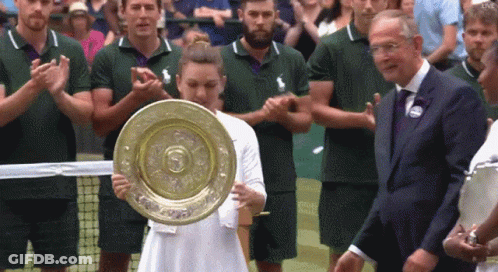 A Woman In A White Dress Holds A Trophy In Front Of A Crowd GIF