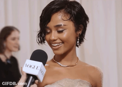 A Woman In A White Dress Is Being Interviewed By A Vogue Microphone GIF