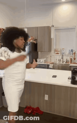 A Woman In A White Dress Is Dancing In A Kitchen GIF