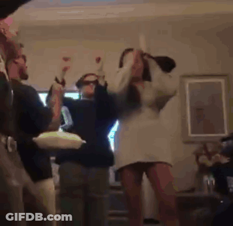 A Woman In A White Dress Is Dancing In A Living Room With Other People . GIF