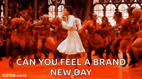 A Woman In A White Dress Is Dancing In Front Of A Crowd With The Words " Can You Feel A Brand New Day " Below Her GIF