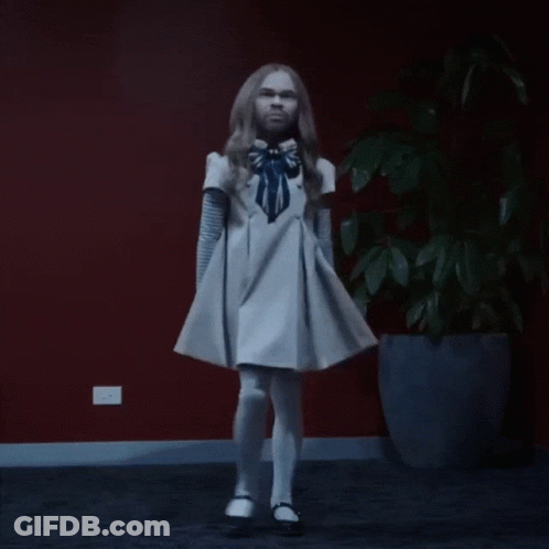 A Woman In A White Dress Is Dancing In Front Of A Potted Plant GIF