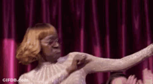 A Woman In A White Dress Is Dancing In Front Of A Red Curtain . GIF