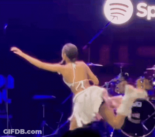A Woman In A White Dress Is Dancing On A Stage In Front Of A Spotify Logo GIF