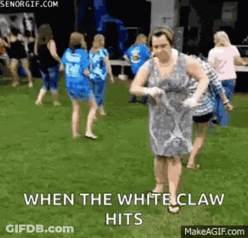 A Woman In A White Dress Is Dancing On The Grass With A Group Of People . GIF