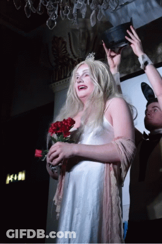 A Woman In A White Dress Is Holding A Bouquet Of Red Flowers GIF
