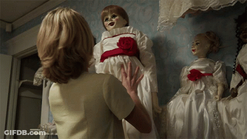 A Woman In A White Dress Is Holding A Doll With A Red Rose On It GIF