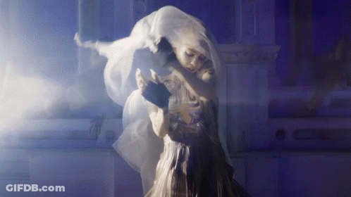 A Woman In A White Dress Is Hugging Another Woman In A Dark Room GIF