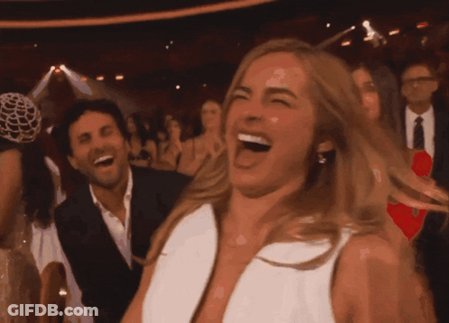 A Woman In A White Dress Is Laughing In A Crowded Room GIF