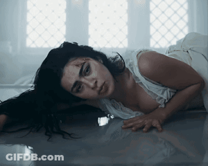 A Woman In A White Dress Is Laying On The Floor Looking At The Camera GIF