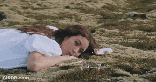 A Woman In A White Dress Is Laying On The Grass GIF