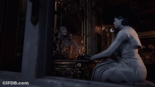 A Woman In A White Dress Is Looking At Herself In A Mirror GIF