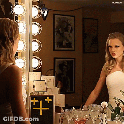 A Woman In A White Dress Is Looking At Herself In A Mirror With 4K Taylor Written On The Bottom GIF