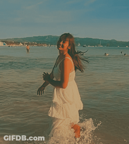 A Woman In A White Dress Is Running Into The Water GIF