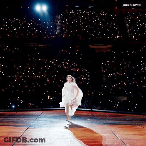 A Woman In A White Dress Is Running On A Stage With Swifterpics Written On The Bottom Of The Image GIF