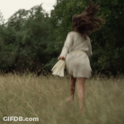 A Woman In A White Dress Is Running Through Tall Grass GIF
