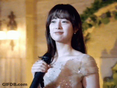 A Woman In A White Dress Is Singing Into A Microphone . GIF