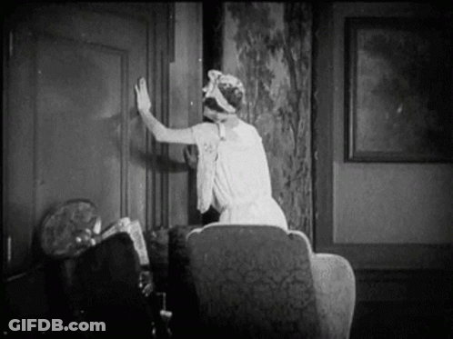 A Woman In A White Dress Is Sitting In A Chair In A Living Room . GIF