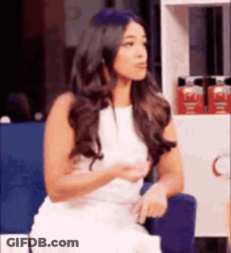 A Woman In A White Dress Is Sitting In A Chair In Front Of A Shelf . GIF