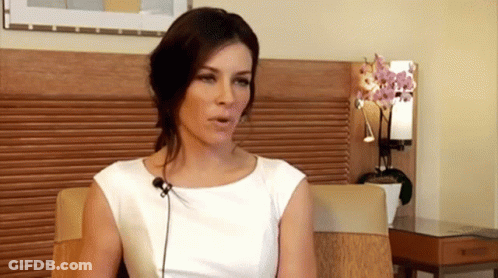A Woman In A White Dress Is Sitting In A Chair With A Microphone In Front Of Her GIF