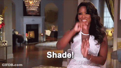 A Woman In A White Dress Is Sitting In A Living Room Clapping Her Hands And Says Shade . GIF