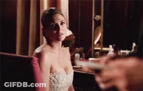 A Woman In A White Dress Is Sitting In Front Of A Mirror Looking At The Camera . GIF