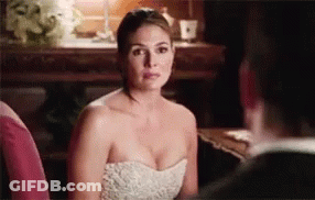 A Woman In A White Dress Is Sitting Next To A Man In A Suit And Looking At Him . GIF
