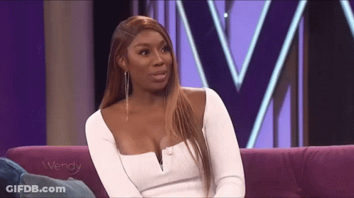 A Woman In A White Dress Is Sitting On A Purple Couch And Talking To Someone . GIF